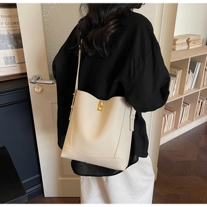 Détail du sac seau beige clair montrant le cuir grainé et le fermoir doré sur modèle