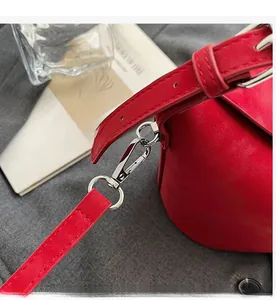 Detail of silver swivel hook on red suede shoulder bag with polished metallic finish