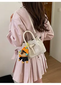 Detail of beige canvas mini bucket bag with leather handle and cute dog charm on model