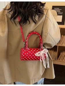 Red polka dot cylinder bag with lace bow and pearl charm shown on model in warm setting