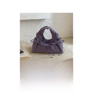 Dettaglio borsa a mano viola in pelle con fiocchi decorativi su base in pietra