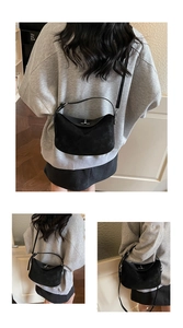 Detailed close-up of a minimalist black suede shoulder bag featuring a silver metal clasp