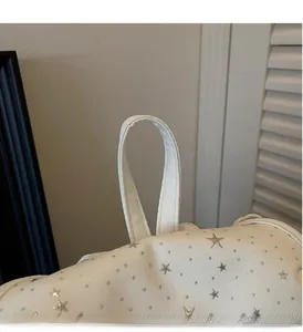 Close-up of white canvas backpack handle featuring silver star decorative details