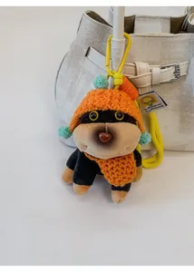 Close-up of a cute black plush puppy keychain with orange knit hat on a white handbag
