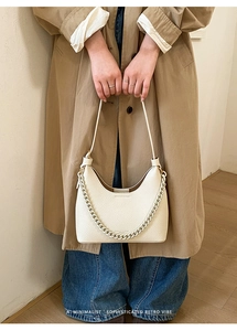 Detail showing creamy white litchi grain leather texture and metallic chain on the handbag