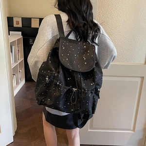 Black drawstring backpack with white star pattern worn by model in a library setting