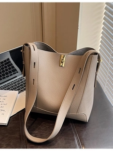Sac seau en cuir grainé taupe avec fermoir tournant doré posé sur un bureau