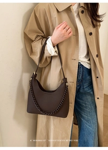 Close-up of dark brown lychee leather crescent bag with vintage metal chain on model