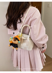 Detail of minimalist beige textured bucket bag featuring a cute dog plush pendant on handle
