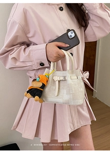 Detail of cream textured handbag with leather strap buckle and cute bear charm accent