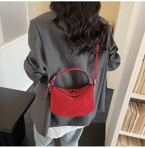 Detail view of the red matte leather half-moon bag on a model in a casual indoor setting