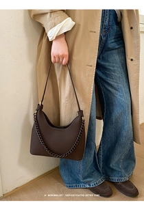 Detail of dark coffee litchi grain leather hobo bag with gold chain and strap on trench coat