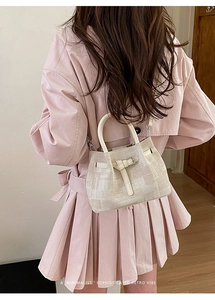 Detail of beige textured bucket bag with top handle and strap on elegant trench coat