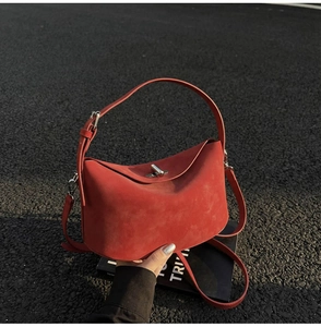 Detail view of red suede bucket bag featuring silver metal twist lock and adjustable strap