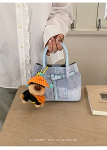 Detail of light blue denim bucket bag with a cute plush puppy charm on a wooden table