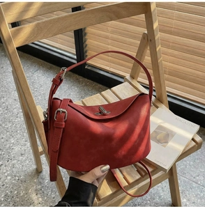 Detail of red matte leather bucket bag with silver clasp on a wooden chair