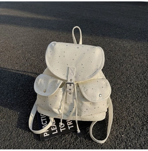 Detail of white canvas backpack featuring silver star prints and metallic buckle pockets