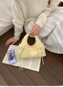 Dettaglio della borsa a mano plissettata giallo crema con fiocchi laterali su un libro