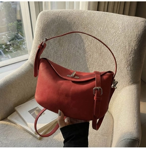 Detailed close-up of a red leather underarm bag featuring a metallic buckle and matte finish