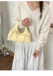 Dettaglio borsa in pelle giallo tenue con fiocchi decorativi portata da una modella