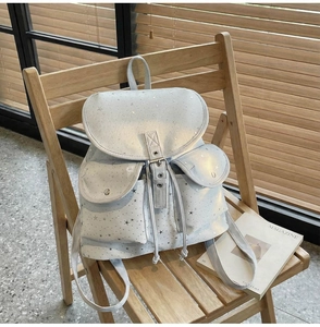 Detail of light gray backpack with silver stars on a wooden chair with magazine