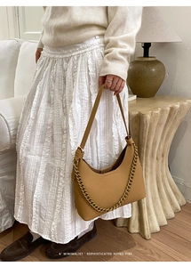 Minimalist brown leather crescent bag with gold chain strap in a retro interior setting