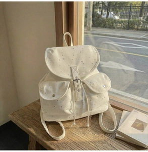 Detailed close-up of a cream canvas backpack with silver star prints on a wooden bench