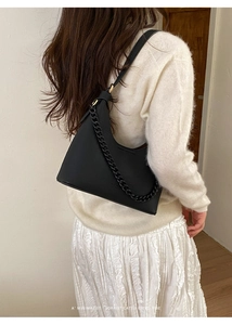Detail of black pebbled leather hobo bag with chain strap styled on a white knit sweater