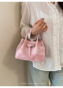 Detail of pink textured handbag with metal buckle strap worn by a model in casual outfit