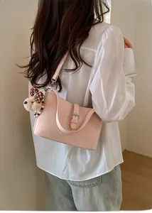Detail view of pink PU leather shoulder bag with buckle and plush dog charm on a model