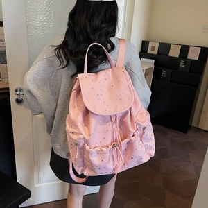 Pink polka dot drawstring backpack with silver stars on female model in indoor setting
