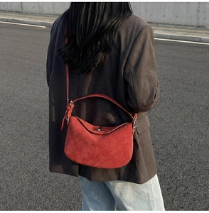 Street style shot of a red suede bucket bag paired with a minimalist grey suit jacket