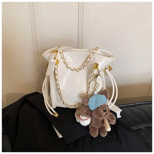 Detailed macro of white quilted bucket bag with gold chain strap and teddy bear charm