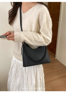 Detail of minimalist black pebbled leather handbag with decorative thick chain and strap