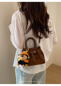 Detail of dark brown suede bucket bag with round handle and cute dog plush pendant