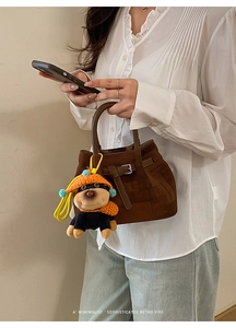 Detail view of brown suede handbag with a cute dog plush charm and silver hardware