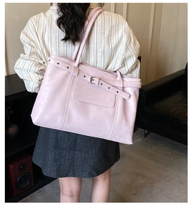 Detail of pink tote bag with metal buckle strap worn on shoulder by a female model