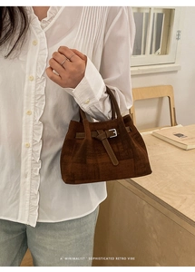 Detail of dark brown suede bucket bag with decorative buckle and vintage textured finish