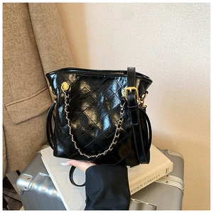 Close-up of quilted pattern and gold chain strap on a black glossy leather bucket bag