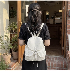 Detail of a beige canvas backpack featuring silver star prints and metal buckle closures