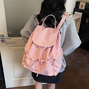 Pink drawstring backpack with silver star patterns shown on a model in a cozy setting