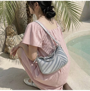 Minimalist light gray leather bucket bag with silver metal buckle held by model at poolside
