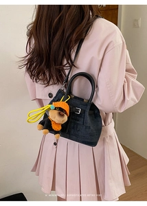 Detail of black denim bucket bag with plush dog charm worn by a model in pink dress