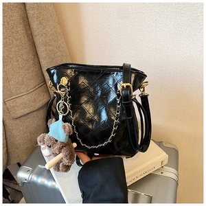 Detail of black quilted chain shoulder bag with cute bear charm and golden hardware