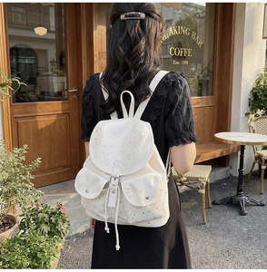 Detail view of cream canvas backpack featuring star patterns and drawstring flap closure