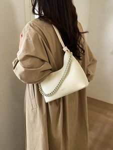 Close-up of beige lychee texture leather bag with chain handle on trench coat