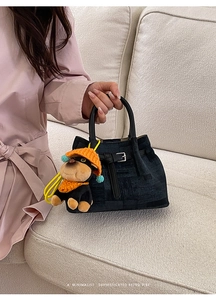 Close-up of black textured handbag with metal buckle and cute dog plush pendant charm
