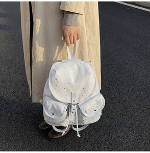 Close-up of white star print backpack with dual front pockets and drawstring closure detail