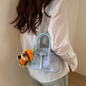 Detail of light blue textured tote bag with a cute puppy plush charm and leather handles