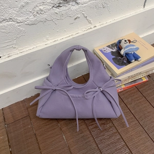 Borsa a mano plissettata viola chiaro con fiocco su pavimento in legno con peluche